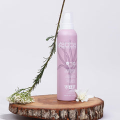 ABBA Volume Foam Styling Mousse 8 oz bottle displayed on a wood slice with flowers and greenery