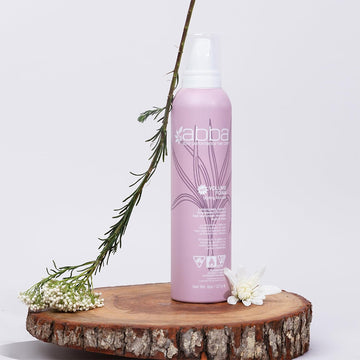 ABBA Volume Foam Styling Mousse 8 oz bottle displayed on a wood slice with flowers and greenery