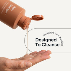 Loma Daily Shampoo dispensed from an open orange bottle onto a hand, demonstrating its lightweight texture
