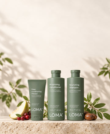 LOMA Deep Conditioning Masque, Nourishing Conditioner, and Nourishing Shampoo on a stone platform with fruit and green leaves