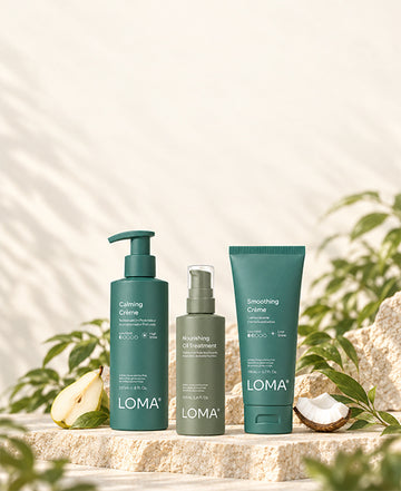 LOMA Calming Crème, Nourishing Oil Treatment, and Smoothing Crème on a stone platform with pear and coconut