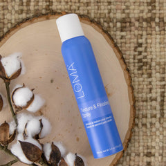 Loma Texture & Finishing Spray 5.4 oz blue aerosol can arranged on a wooden slice with cotton flowers
