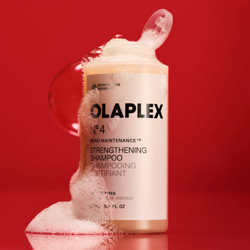 OLAPLEX Nº.4 Bond Maintenance Strengthening Shampoo in a 17.5 oz bottle surrounded by rich lather against a red background