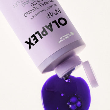 Close-up of OLAPLEX Nº.4P Blonde Enhancer Purple Toning Shampoo dispensing a rich purple formula onto a white surface