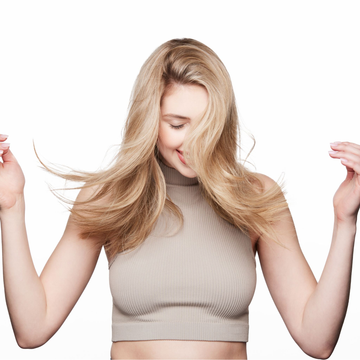 Woman with long blonde hair holding sections of her hair against a white background.