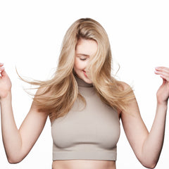 Woman with long, loose blonde hair holding sections of her hair against a white background.
