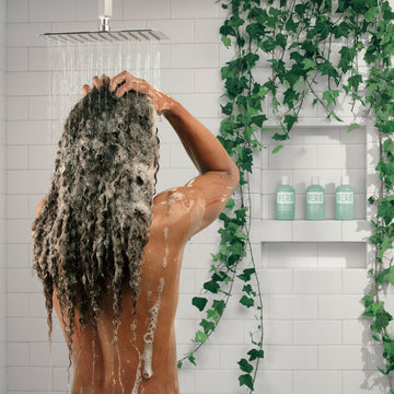 Person massaging Verb Dandruff Shampoo into wet curly hair in a shower