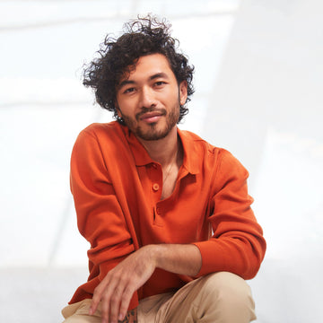Male model with short curly dark hair wearing an orange shirt in a Verb Forming Fiber styling campaign