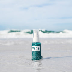 Verb Hydrate Oil 2 oz bottle standing in shallow ocean water with waves in the background