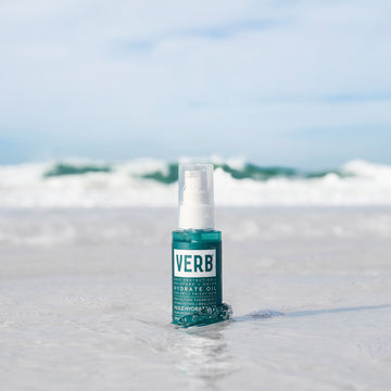 Verb Hydrate Oil 2 oz bottle standing in shallow ocean water with waves in the background