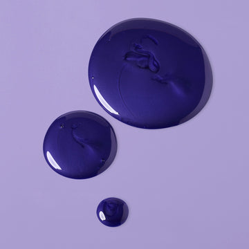 Glossy dark violet Verb Purple Shampoo texture shown in drops on a lavender background